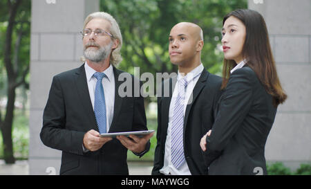 multinational corporate executives standing and looking up in modern office building. Stock Photo