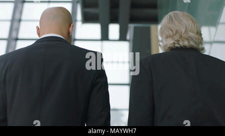 rear view of corporate executives talking while ascending stairs in modern office building. Stock Photo