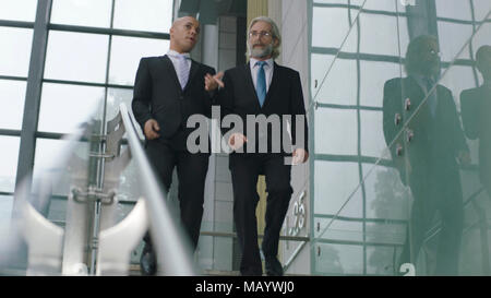 two corporate executives talking while descending stairs in modern office building. Stock Photo