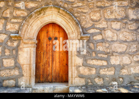 background with old big red dark brown door with arch in a wall of yellow stones Stock Photo