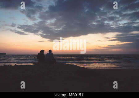 a man and a woman sit on a rock on the shore and look towards the dawn. Sunrise on the Andaman Islands India. silhouette of couple watching sunset on  Stock Photo