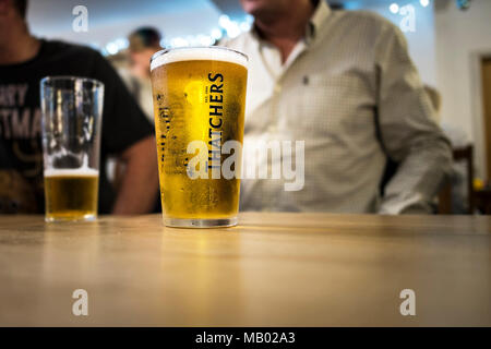 A pint glass of Thatchers Cider on a table in a bar. Stock Photo
