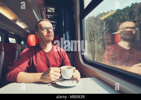 Rail transportation in sunny day. Pensive young man holding a cup of coffee traveling by train. Stock Photo