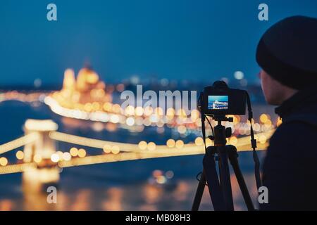 Photographer with tripod. Young man taking photo with his camera in the night city. Budapest, Hungary. Stock Photo