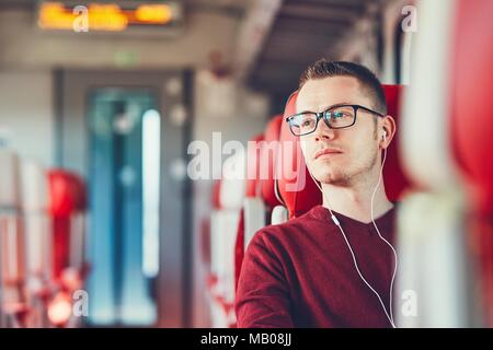 Rail transportation. Thoughtful young man with eyeglasses listening to music while traveling by train. Stock Photo
