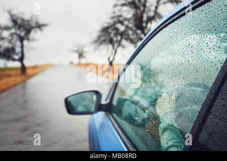 Rainy day on the road. Man is driving car in rain. Selective focus on raindrops. Stock Photo