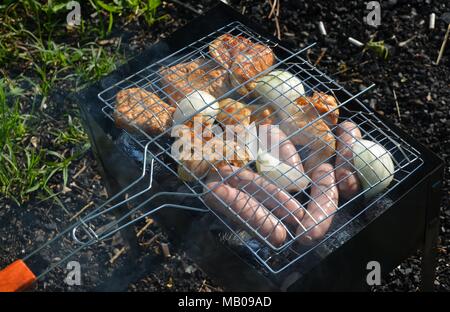 View from above onto a variety of roast meat, chicken, onions potatoes and sausages on a barbecue grill rack Stock Photo