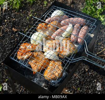 View from above onto a variety of roast meat, chicken, onions potatoes and sausages on a barbecue grill rack Stock Photo