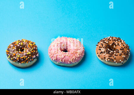 top view of three donuts with multicolored glaze and topping on blue background with copyspace Stock Photo