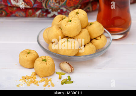 Round shaped Chickpea cookie pastries made of gram flour and pistachio traditional Iranian Sweets: Nokhodchi close up shot and a cup of black tea on t Stock Photo