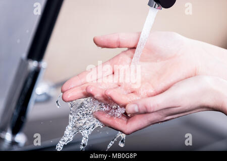 Woman washing or rinsing her hands under running water from a faucet in the kitchen on a metal sink in a close up view Stock Photo