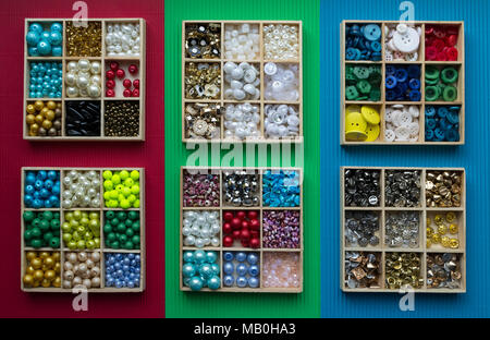 Assortment of clothes buttons in wooden boxes on red, green, blue cardboard background. Variety of colors. View from top Stock Photo
