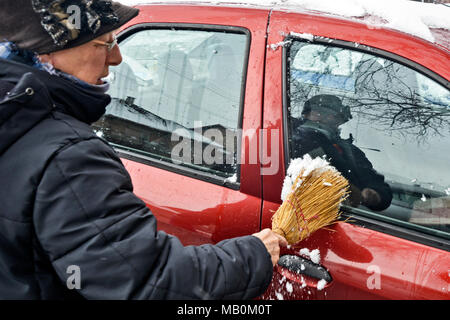 Driver cleaning snow from the windshield of a car using a brush. Stock Photo