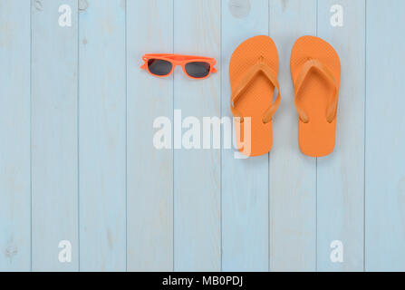 Leisure items on blue wooden background: flip-flops and orange sunglasses Stock Photo