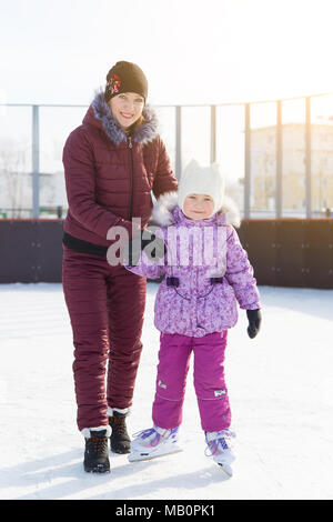 A woman with a little girl on ice learns to skate in the winter. Stock Photo