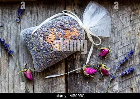 bag with wild roses petals and dried lavender flowers on wooden, vintage background - fragrance to the wardrobe Stock Photo