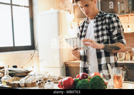Man using tablet and cook dinner, does not understand what is written on the screen. Indoor, studio shot Stock Photo
