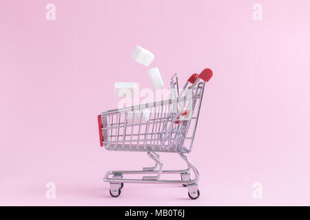 Sugar cubes falling into small shopping cart toy model on pastel pink background minimal creative concept. Stock Photo