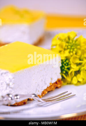 slice of lemon mousse on a white place with a silver fork and yellow flowers bokeh background to ad copy space