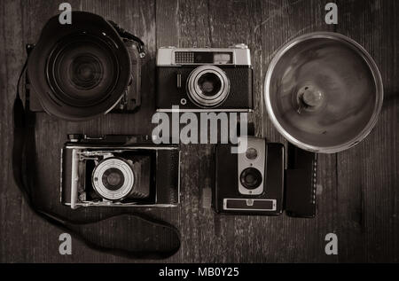 Close up black and white photo of a selection of vintage film cameras with one modern DSLR on a background of weathered wood. Stock Photo