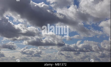 Beautiful billowing rolling clouds in a blue sky on a bright sunny day. The cumulus clouds have a silver lining, with a puffy white top with sun rays. Stock Photo