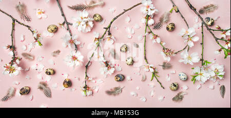 Easter holiday background. Flat-lay of tender Spring almond blossom flowers on branches, feathers, quail eggs over light pink background, top view. Gr Stock Photo