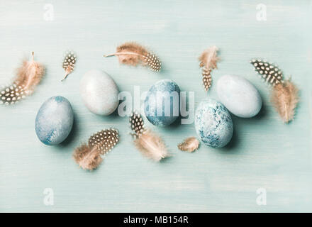 Painted traditional eggs for Easter holiday and feathers over light blue background, top view, horizontal composition Stock Photo