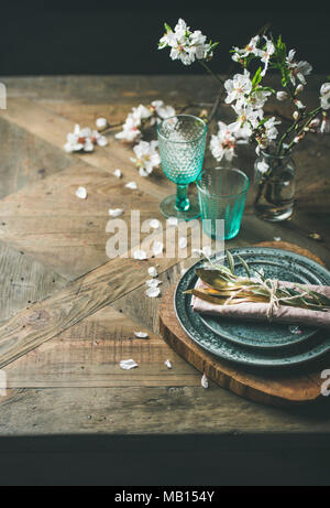 Spring Easter holiday Table setting. Tender almond blossom flowers on branches, plates, glasses and cutlery over vintage wooden table, selective focus Stock Photo