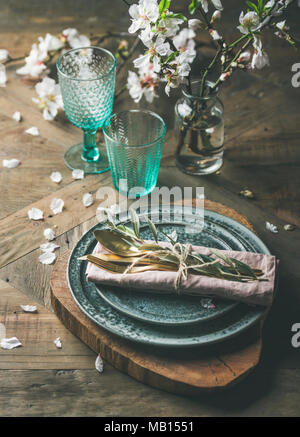 Spring Easter holiday Table setting. Tender almond blossom flowers on branches, plates, glasses and cutlery over vintage wooden table, selective focus Stock Photo