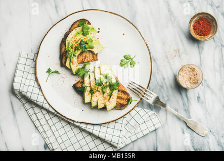 Healthy vegan breakfast or lunch. Flat-lay of avocado toast on plate and seasoning over marble background, top view. Clean eating, detox, weight loss, Stock Photo