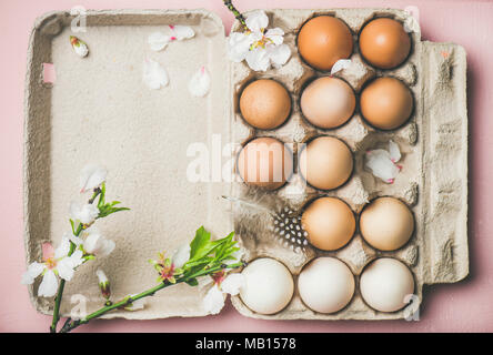 Easter holiday background. Flat-lay of gradient natural colored eggs in box with Spring almond blossom flower branch and feather over pink background, Stock Photo