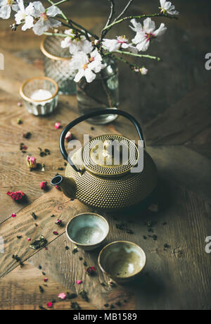 Traditional Asian tea ceremony arrangement. Golden iron teapot, cups, dried rose, candles and almond blossom flowers over vintage wooden table backgro Stock Photo