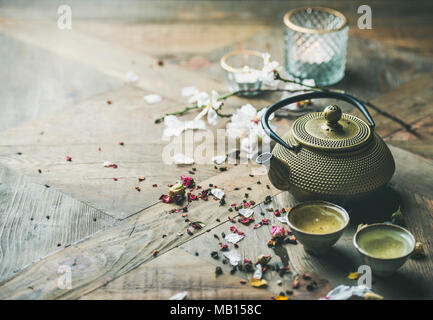 Traditional Asian tea ceremony arrangement. Iron teapot, cups, dried rose buds and candles over wooden table background, selective focus, copy space Stock Photo