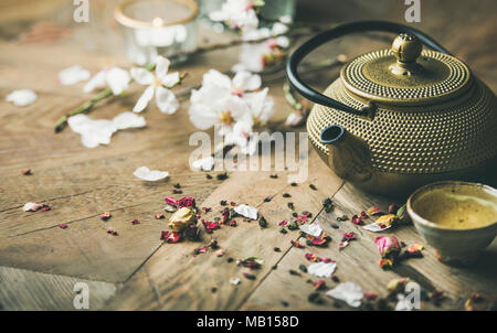 Traditional Asian tea ceremony arrangement. Iron teapot, cups, blooming almond flowers, dried rose buds and candles over wooden table background, sele Stock Photo