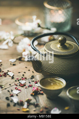 Traditional Asian tea ceremony arrangement. Iron teapot, cups, blooming almond flowers, dried rose buds and candles over wooden table background, sele Stock Photo