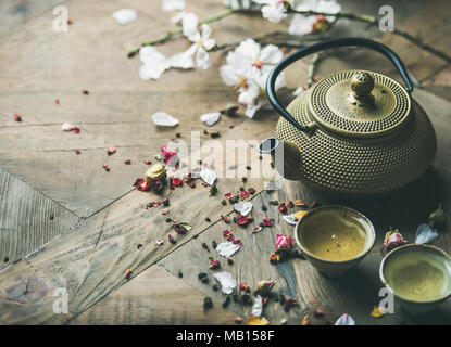 Traditional Asian tea ceremony arrangement. Iron vintahe teapot, cups, blooming almond flowers, dried rose buds and candles over wooden table backgrou Stock Photo