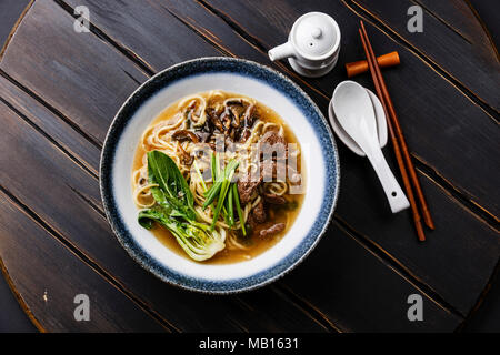 Ramen asian noodle in broth with Beef and Oyster mushrooms in bowl on dark wooden background Stock Photo