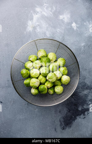 raw Brussels sprouts in colander on concrete background Stock Photo