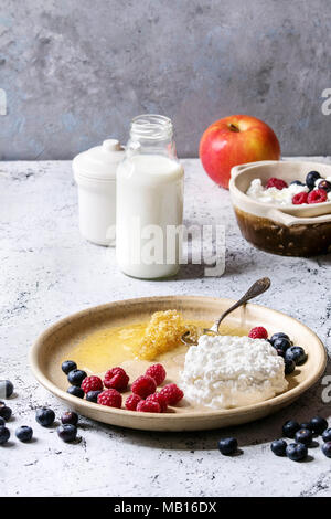 Ceramic plate of homemade cottage cheese served with blueberries, raspberries, bottle of milk and honeycombs over white marble texture table as backgr Stock Photo