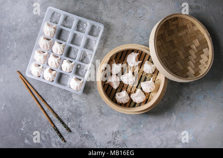 Frozen ready to cook asian potstickers dumplings stuffed by shrimps in plastic box with chopsticks and bamboo steamer over grey texture background. To Stock Photo