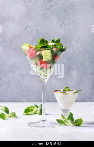 Spring summer diet salad with strawberries, cucumber, green field salad and yogurt mint sauce served in cocktail glass over grey texture background. C Stock Photo