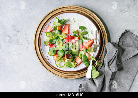 Spring summer diet salad with strawberries, cucumber, green field salad and yogurt mint sauce served in blue plate with cloth napkin over grey texture Stock Photo