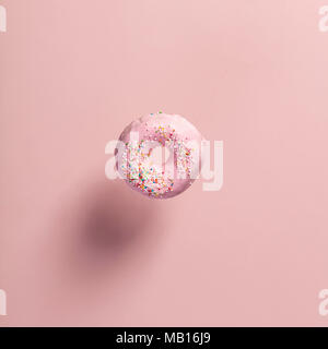 Pink doughnut with sprinkles falling or flying in motion against pink pastel background Stock Photo