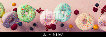 Sweet and colourful doughnuts with sprinkles and berries falling or flying in motion against pink pastel background Stock Photo
