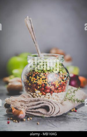 Legumes - lentils chickpeas beans green peas in a glass jar and raw vegetables. Vegan protein source. Vegetarian and healthy food concept Stock Photo