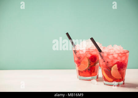 Red drink with ice. Cocktail making bar tools, raspberry, lime, oranges and mint leaves. Raspberry mojito on blue background Stock Photo