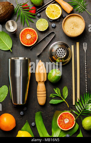 Cocktail making bar tools, shaker, tropical fruits and leaves on a dark background. Top view Stock Photo