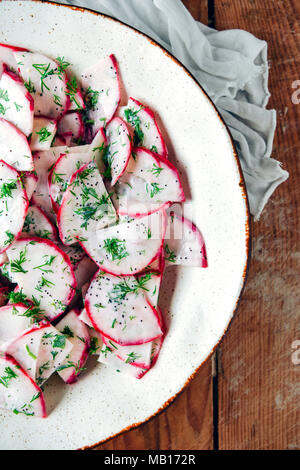 Radish salad with yogurt and poppy seed dressing photographed in a white ceramic bowl on a wooden background from top view. Stock Photo