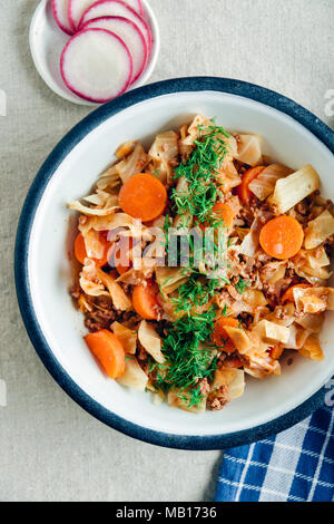 Cabbage stew with ground beef and carrot topped with chopped fresh dill served in a vintage bowl photographed from top view. Sliced radish and a blue Stock Photo
