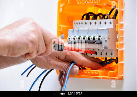 Electrician technician working on a residential electrical panel, fixing with a screwdriver the cable in the magnetothermal switch Stock Photo